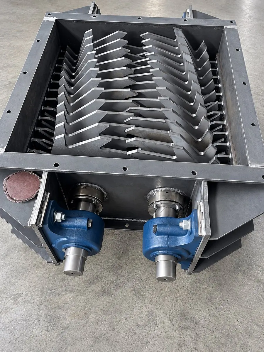 Open cutter box of a twin-shaft shredder, showing the interlocking cutter discs and the two shaft ends with bearing housings