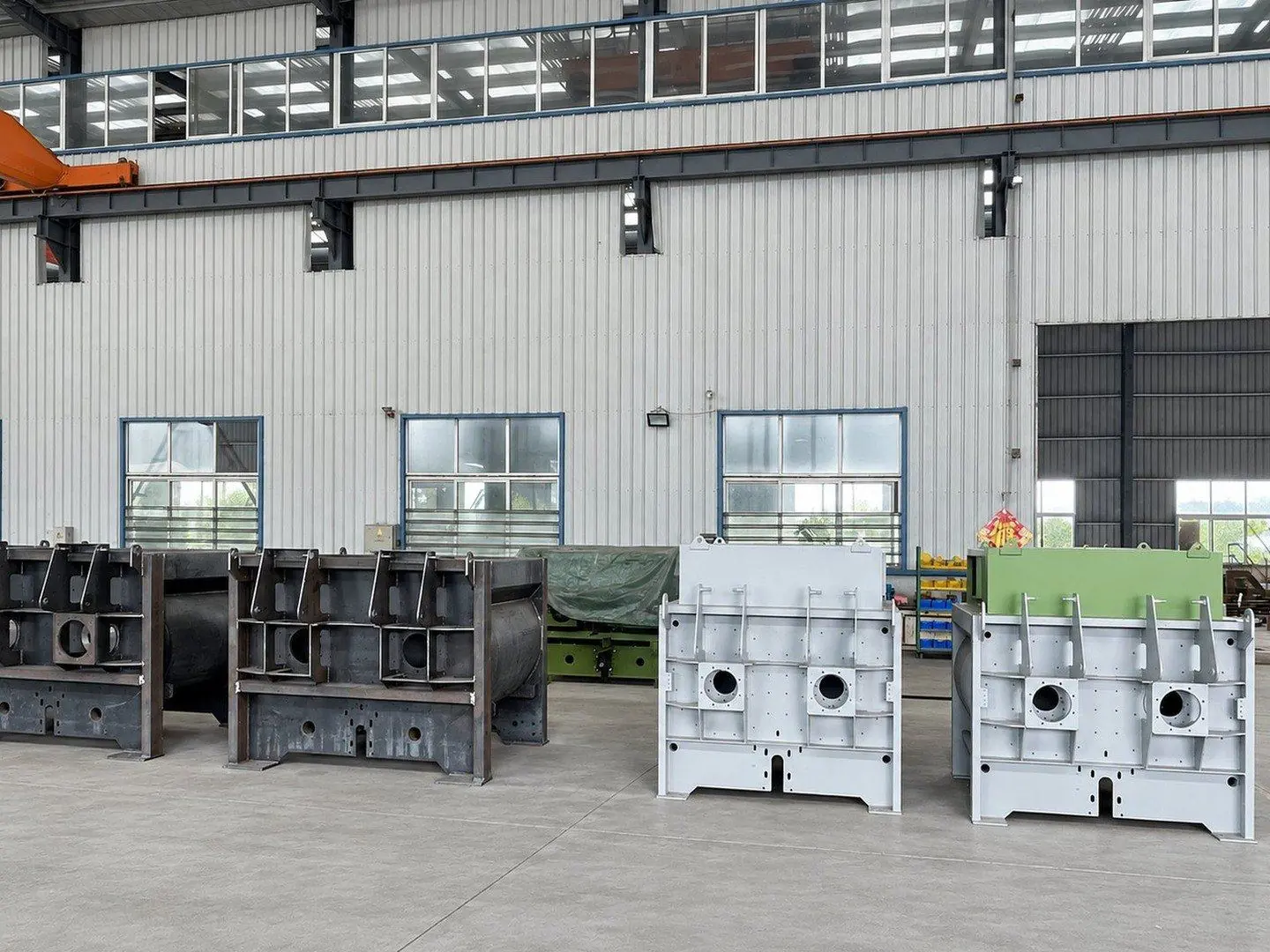 Twin-shaft mixer frames on the workshop floor: bare welded steel, primed grey and painted green